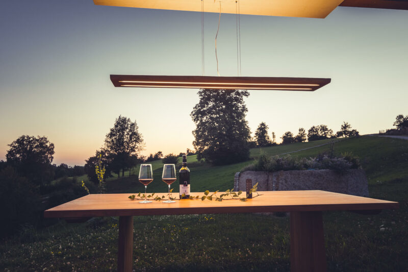 Lichten Lampe aus Eichenholz in abgehängter Variante über einem Tisch mit Wein und Weingläsern